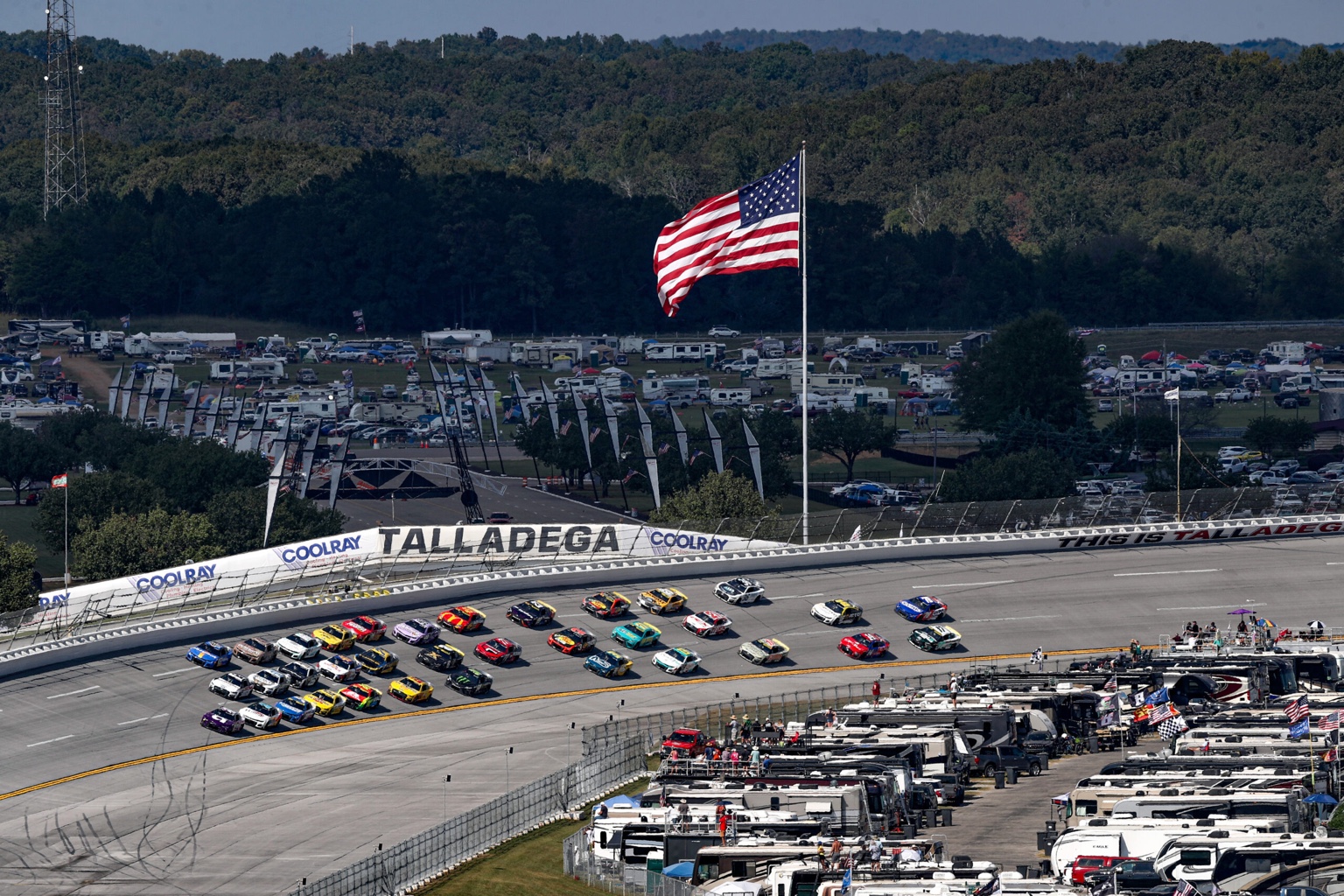 Race cars at Talladega Superspeedway with RV campsites and an American flag overlooking the track